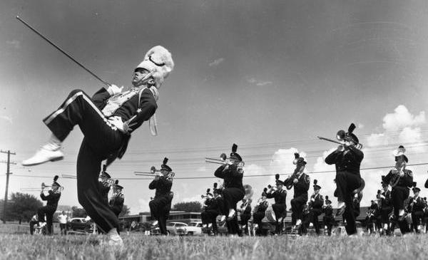 A black and white photo showing a marching band performing outside